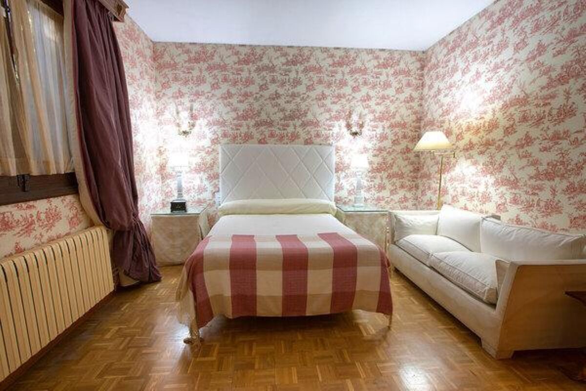 A bedroom with a bed, a sofa, a nightstand, and a lamp.