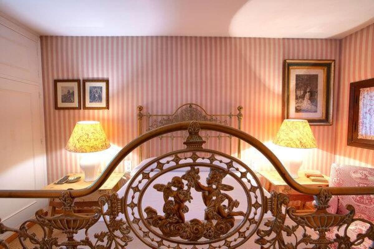 A bedroom with a bed, two bedside lamps, and a wall with striped wallpaper and framed pictures.