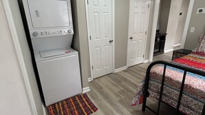 Une chambre à coucher de taille modeste, équipée d’un lave-linge, d’un lit recouvert d’une couvre-lit à motifs et d’un petit tapis.