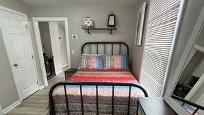 Une chambre à coucher avec un lit, une commode, une horloge et une fenêtre avec des stores.