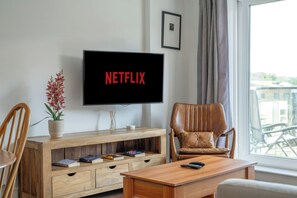 A living room with a television displaying 'NETFLIX,' a wooden entertainment unit with books, a potted plant, and a leather armchair.