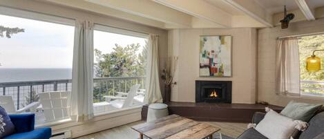 A spacious living room with a fireplace, large windows offering a view of the sea, and a cozy seating area.
