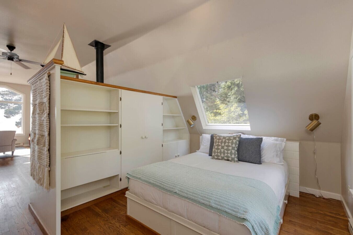 A bedroom with a loft bed, built-in shelving, a skylight, and a ceiling fan.