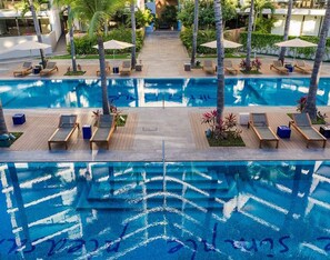 Un espace piscine doté de plusieurs chaises longues et de parasols, entouré de palmiers et de verdure.