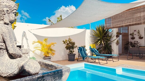 Un área de piscina con una estatua, sillas de descanso y plantas en macetas.