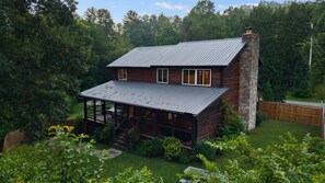 A cabin with a porch, a stone chimney, and a fenced yard.