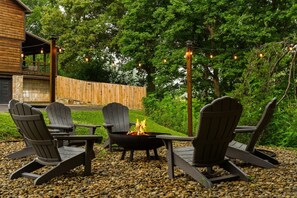 An outdoor seating area with Adirondack chairs, a fire pit, and string lights.