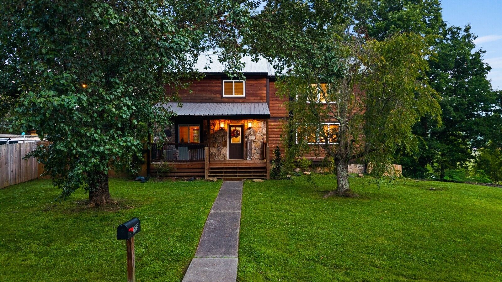 A wooden cabin with a porch, surrounded by a well-maintained lawn and trees.