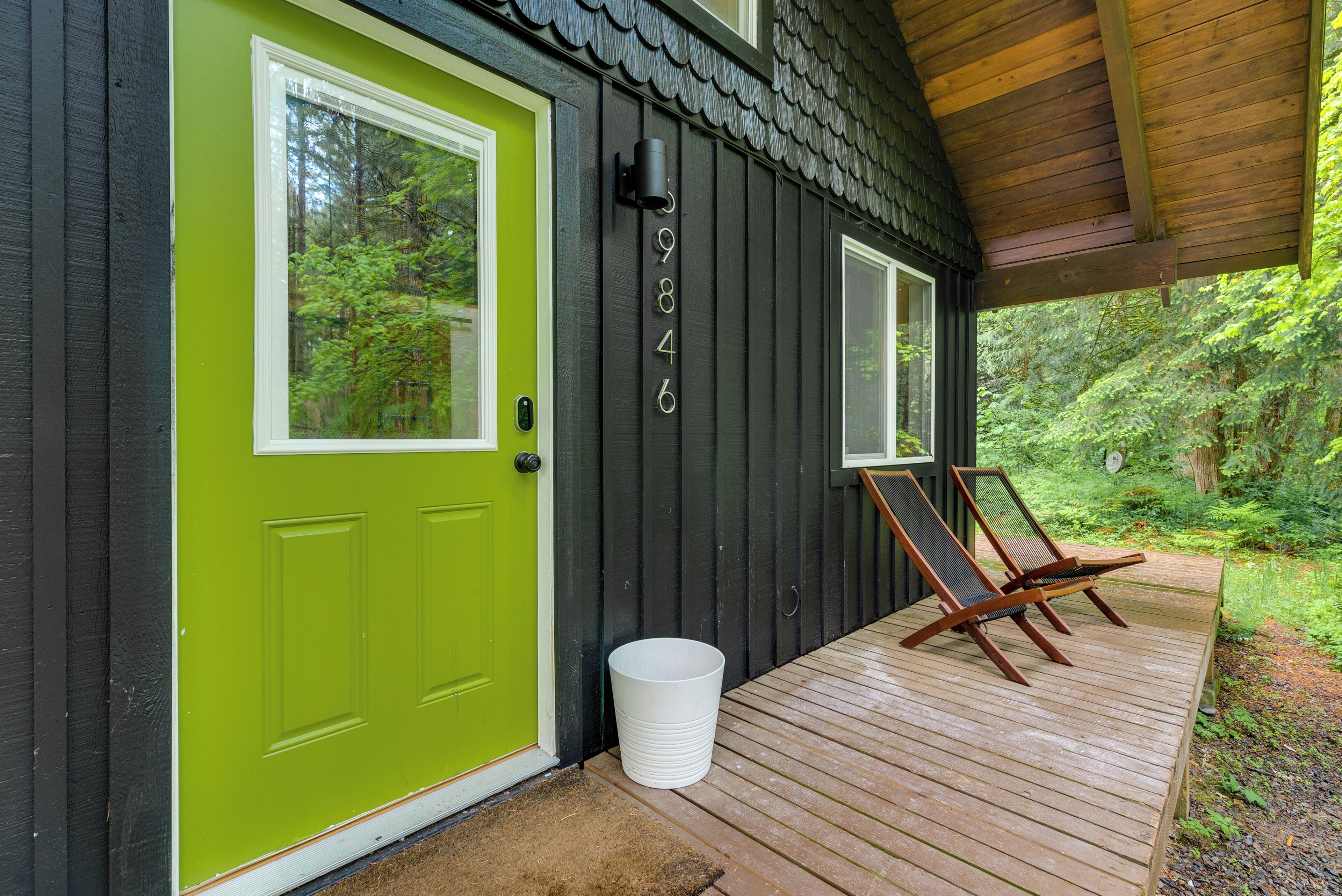 A wooden deck with two lounge chairs, a green door, and a mailbox on a house with a dark exterior.