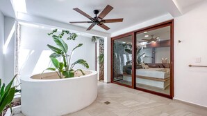 A spacious room with a large white planter, a ceiling fan, and a sliding glass door leading to a bathroom. - Beautiful 6BR mid-island w/private pool (Isla Mujeres)