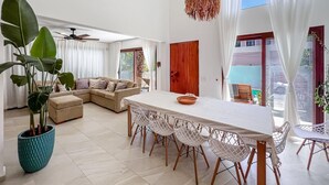 A spacious living area with a large sofa, a dining table with chairs, and a potted plant. - Beautiful 6BR mid-island w/private pool (Isla Mujeres)