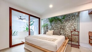 A bedroom with a large bed, a stone wall, and a sliding glass door leading to a balcony. - Beautiful 6BR mid-island w/private pool (Isla Mujeres)