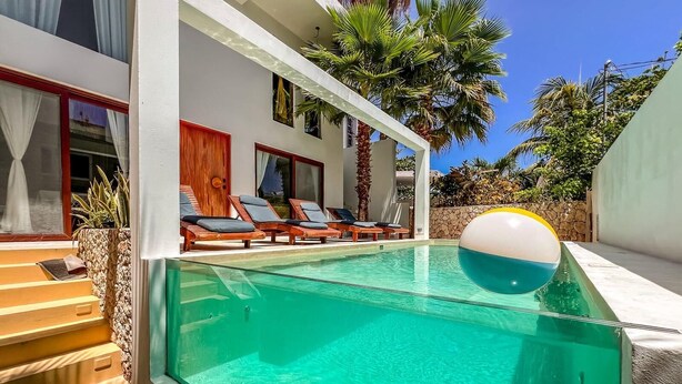 A swimming pool with clear water, surrounded by a white building with a covered patio area. - Beautiful 6BR mid-island w/private pool (Isla Mujeres)