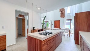 A modern kitchen with a central island, wooden cabinets, and a dining area with a table and chairs. - Beautiful 6BR mid-island w/private pool (Isla Mujeres)