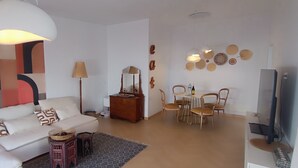 Un salón moderno con un sofá blanco, una mesa de comedor con sillas, un televisor y decoración en la pared.