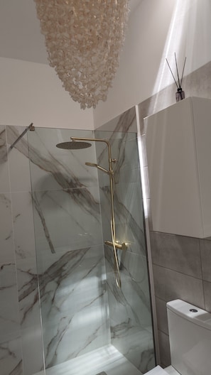 Ein modernes Badezimmer mit einer gläsernen Duschkabine, Marmorfliesen und einer weißen Toilette.