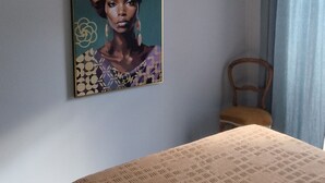 Un dormitorio con cama, lámpara colgante, una silla y un cuadro en la pared.