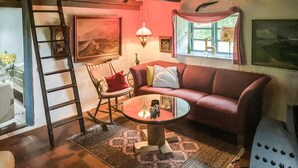 Ein gemütliches Wohnzimmer mit einem roten Sofa, einem Schaukelstuhl, einem Glastisch und einer Leiter an der Wand.