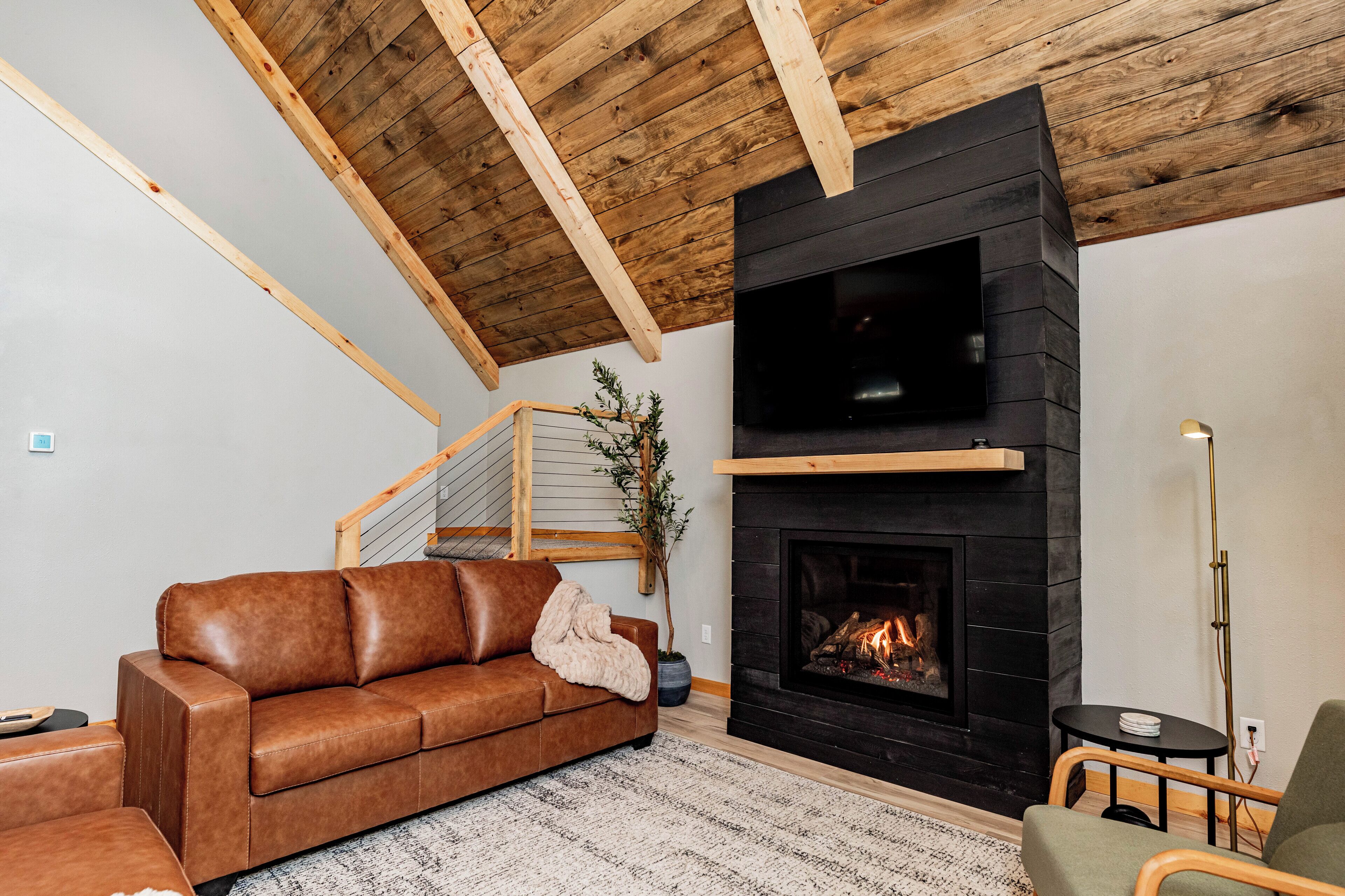 A cozy living room with a brown leather sofa, a fireplace, and a wooden ceiling.