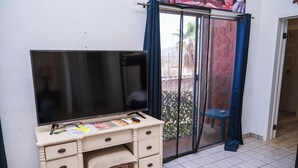 Ein Zimmer mit einem großen Flachbildfernseher auf einer weißen Kommode, einem kleinen Tisch mit blauem Stuhl und einer Glastür mit blauen Vorhängen.