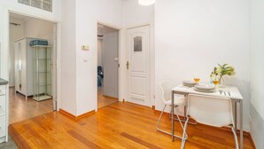 A modern room with a dining table, chairs, and a pendant light. There is a door leading to another room and a closet with a glass door.