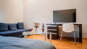 A modern hotel room with a sofa, a glass table with drinks, a TV, and a desk.