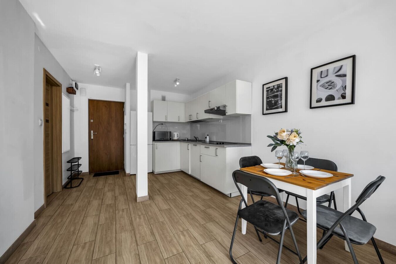 Une cuisine moderne avec des meubles blancs, une table à manger en bois et des chaises noires.