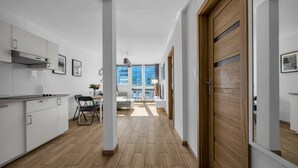 A modern kitchen with white cabinetry, a dining area with a table and chairs, and a view of the city through large windows. - Rondo ONZ Apt - 11th Floor, Top location, Metro - by Rentujemy (Warszawa)