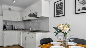 A modern kitchen with white cabinets, a built-in oven, and a microwave. There is a dining table set with plates, glasses, and a vase of flowers. - Rondo ONZ Apt - 11th Floor, Top location, Metro - by Rentujemy (Warszawa)