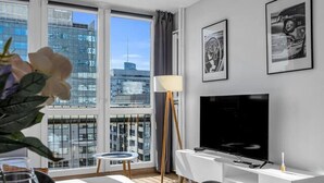 A modern living room with a dining area, large windows, a flat-screen TV, and artwork on the walls. - Rondo ONZ Apt - 11th Floor, Top location, Metro - by Rentujemy (Warszawa)
