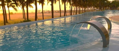A swimming pool with a curved edge, surrounded by palm trees and a beach in the background.
