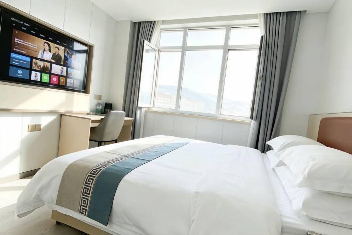 Una habitación de hotel con cama, escritorio, televisor y ventana con cortinas.