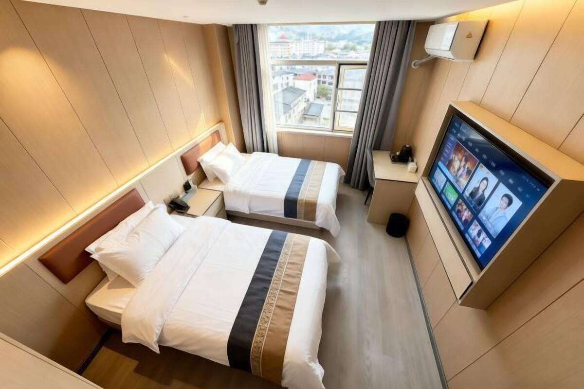 Habitación de hotel con dos camas, televisión y ventana con vista a la ciudad.