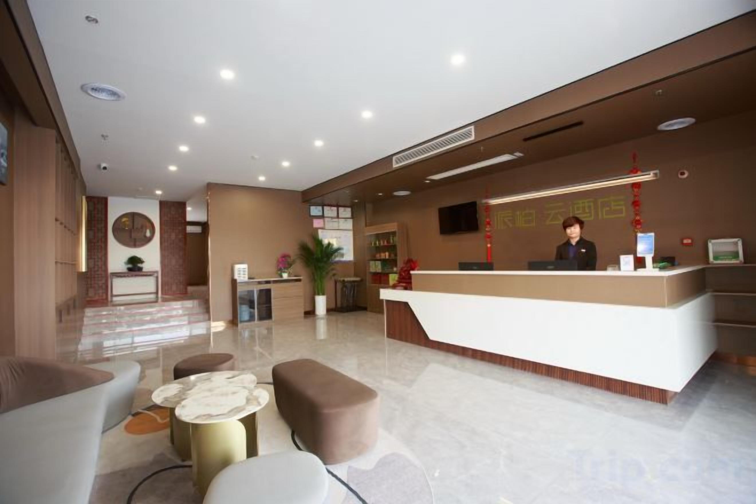A hotel reception area with a reception desk, seating area, and a staircase leading to an upper floor.