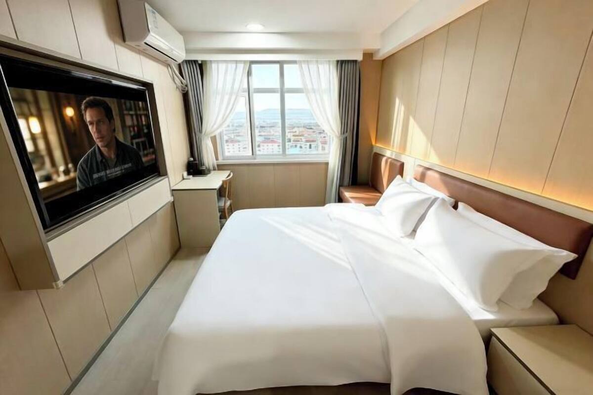 Habitación de hotel con cama, televisión, escritorio y ventana con cortinas.