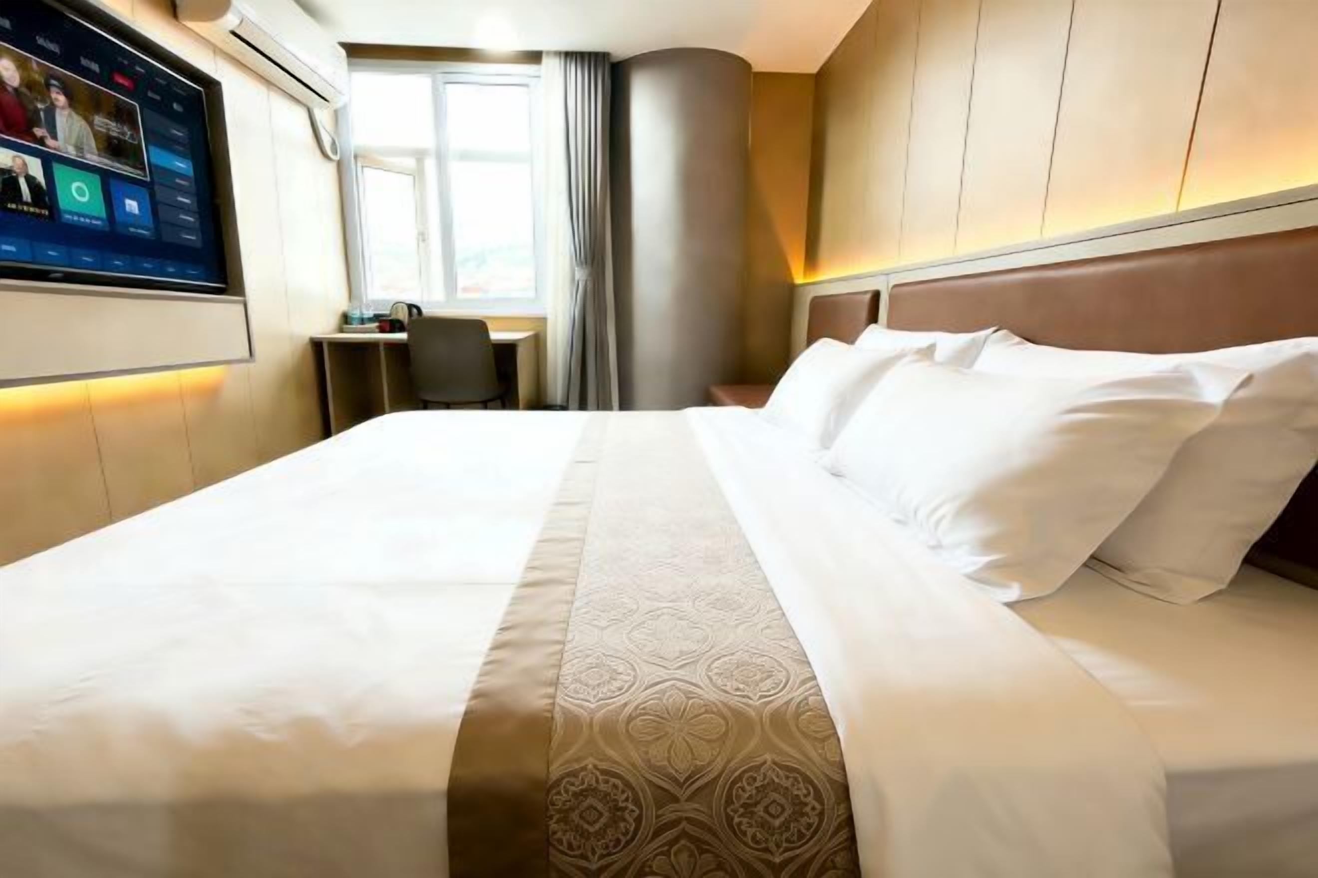 A hotel room with a large bed, a desk, and a television screen displaying a news channel.