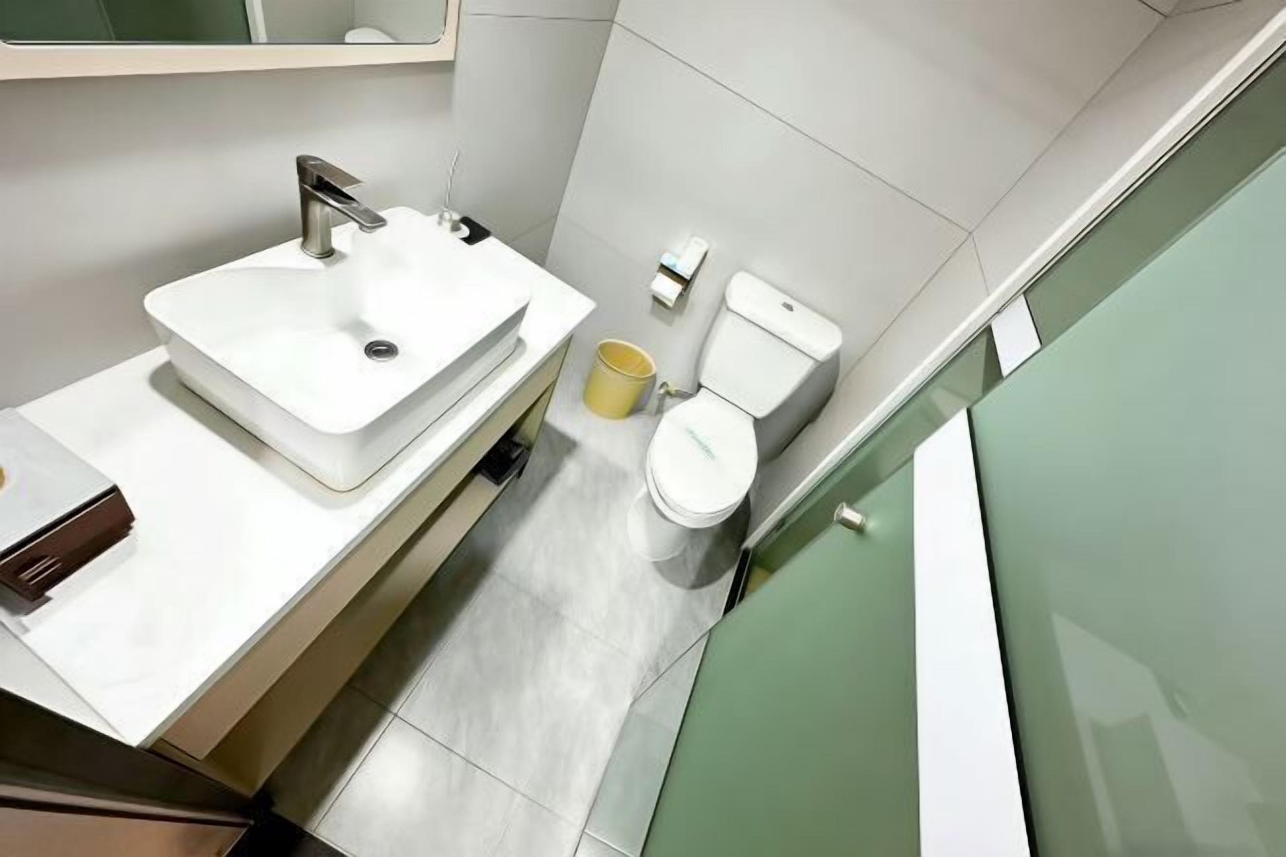 A modern bathroom with a white sink, toilet, and a yellow bucket.
