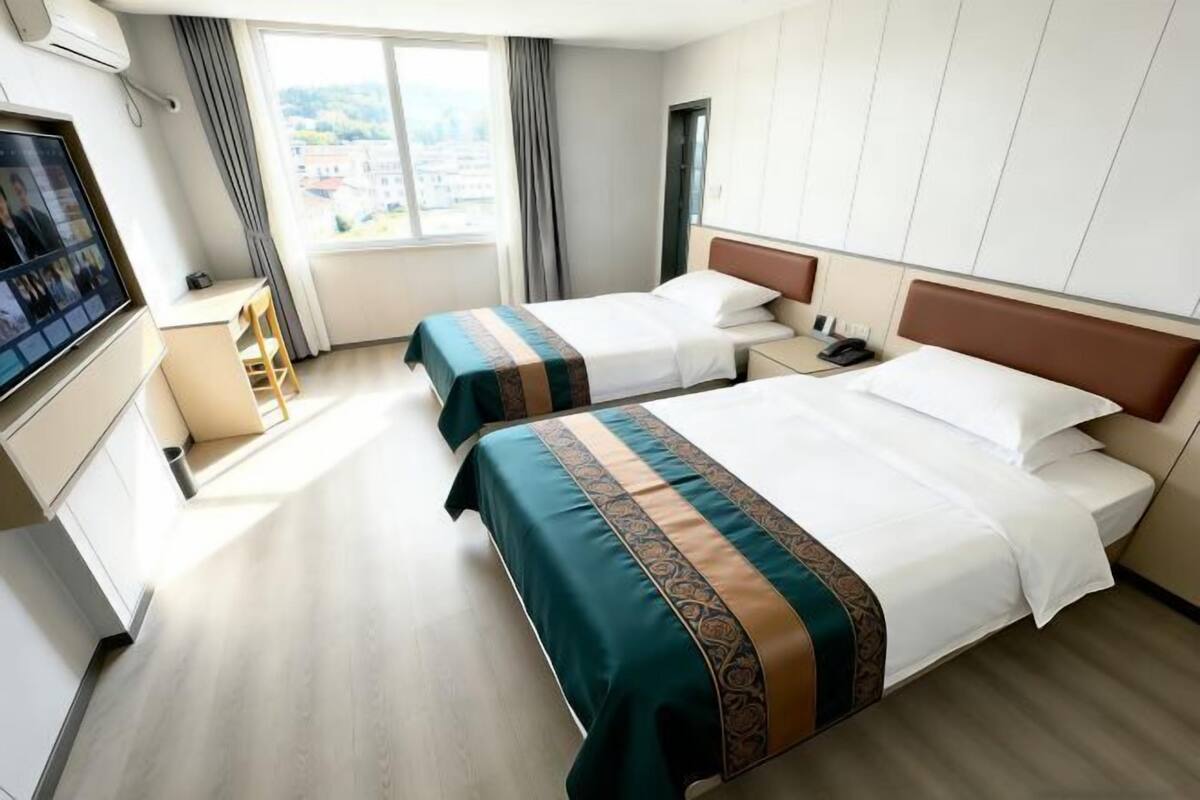 Habitación de hotel con dos camas, un escritorio, una silla, un televisor y una ventana con cortinas.
