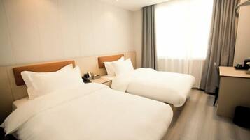 A hotel room with two beds, a desk, and a window with curtains.