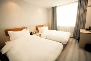 Habitación de hotel con dos camas, un escritorio y una ventana con cortinas.
