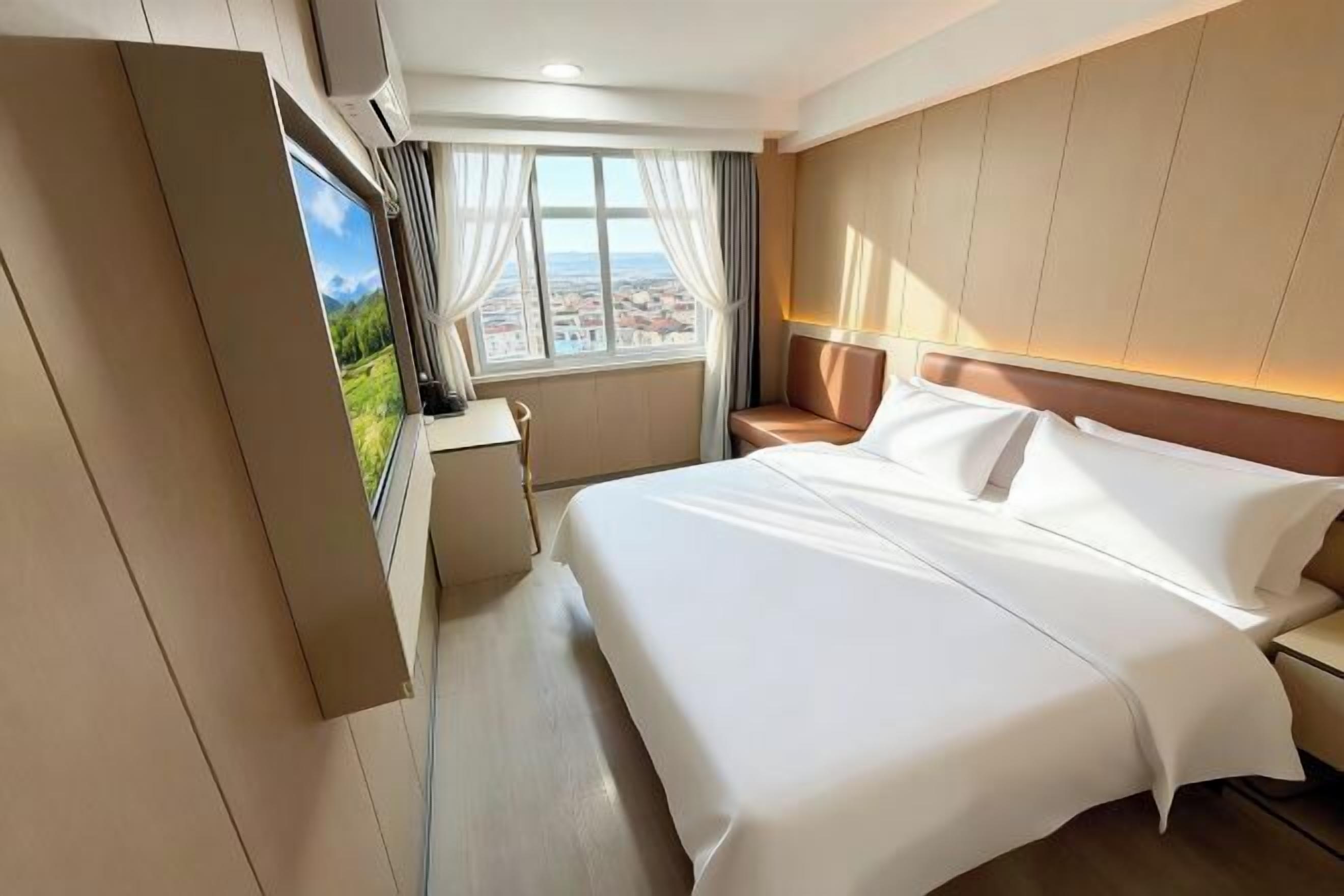 Habitación de hotel con cama, escritorio, silla, ventana con cortinas y vistas a la ciudad.
