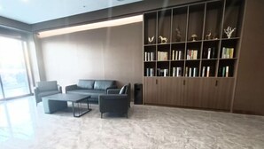 A modern living room with a sofa, two armchairs, a coffee table, and a large bookshelf filled with books and decorative items. - Homeinn Pebble Hotel (Tongling Zhidicheng Fortune Plaza Third Middle School) (Tongling)