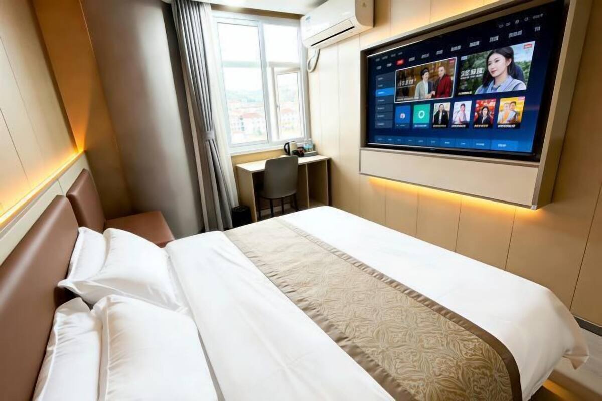 Habitación de hotel con cama, escritorio y televisor en la pared mostrando un programa.