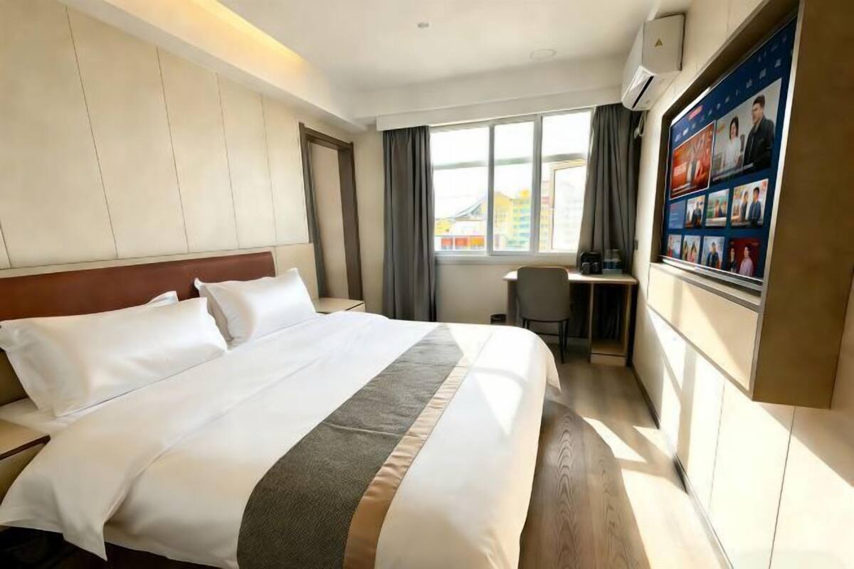 Habitación de hotel con cama, escritorio, silla, ventana con cortinas y televisor instalado en la pared.