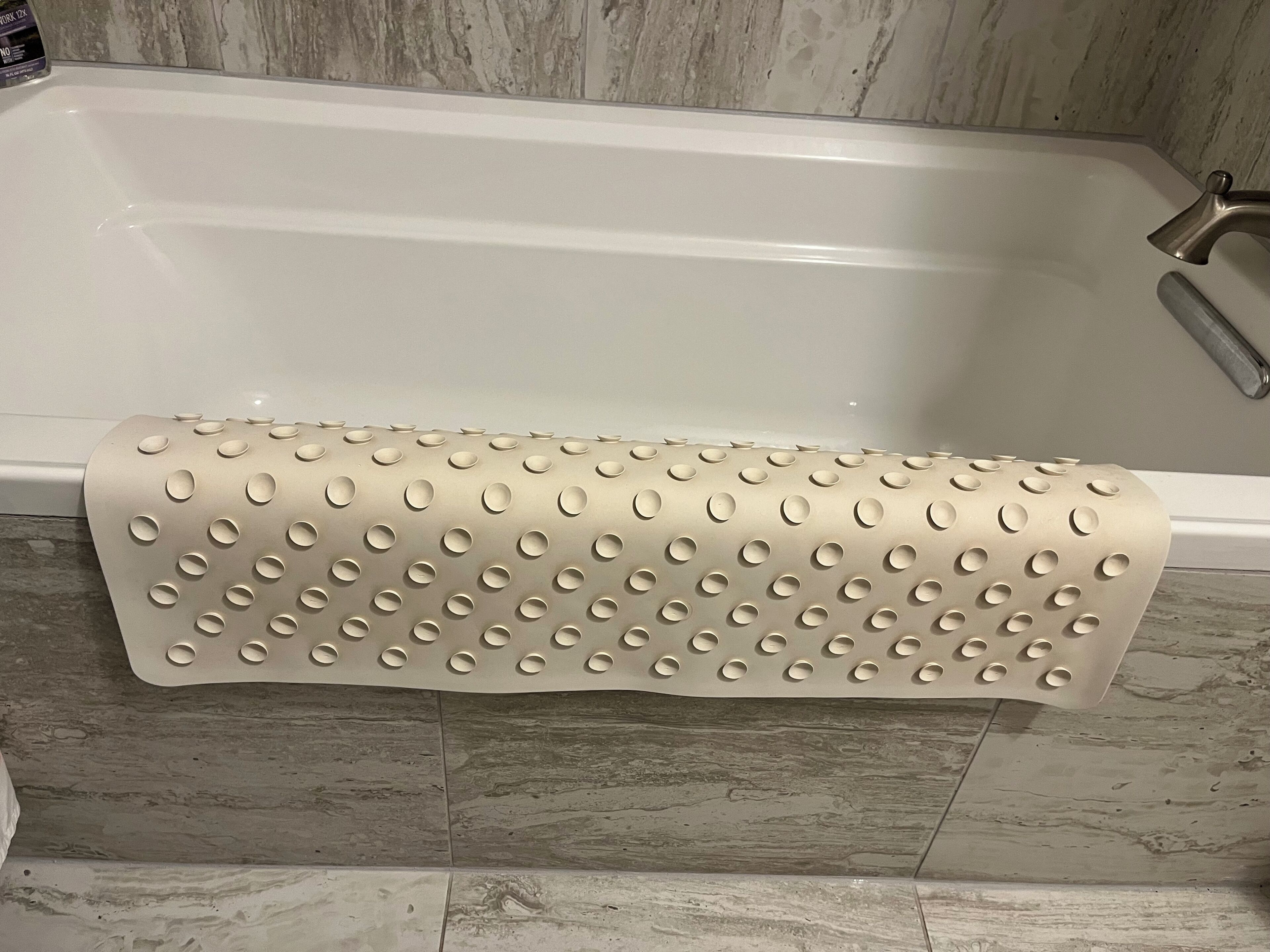 A bathtub with a textured, perforated bath mat.