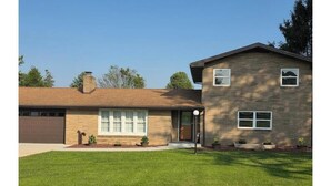 A two-story house with a garage, a front lawn, and a small garden area. - Home away from home (Indiana)
