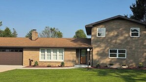 A two-story house with a garage, a front lawn, and a small garden area. - Home away from home (Indiana)