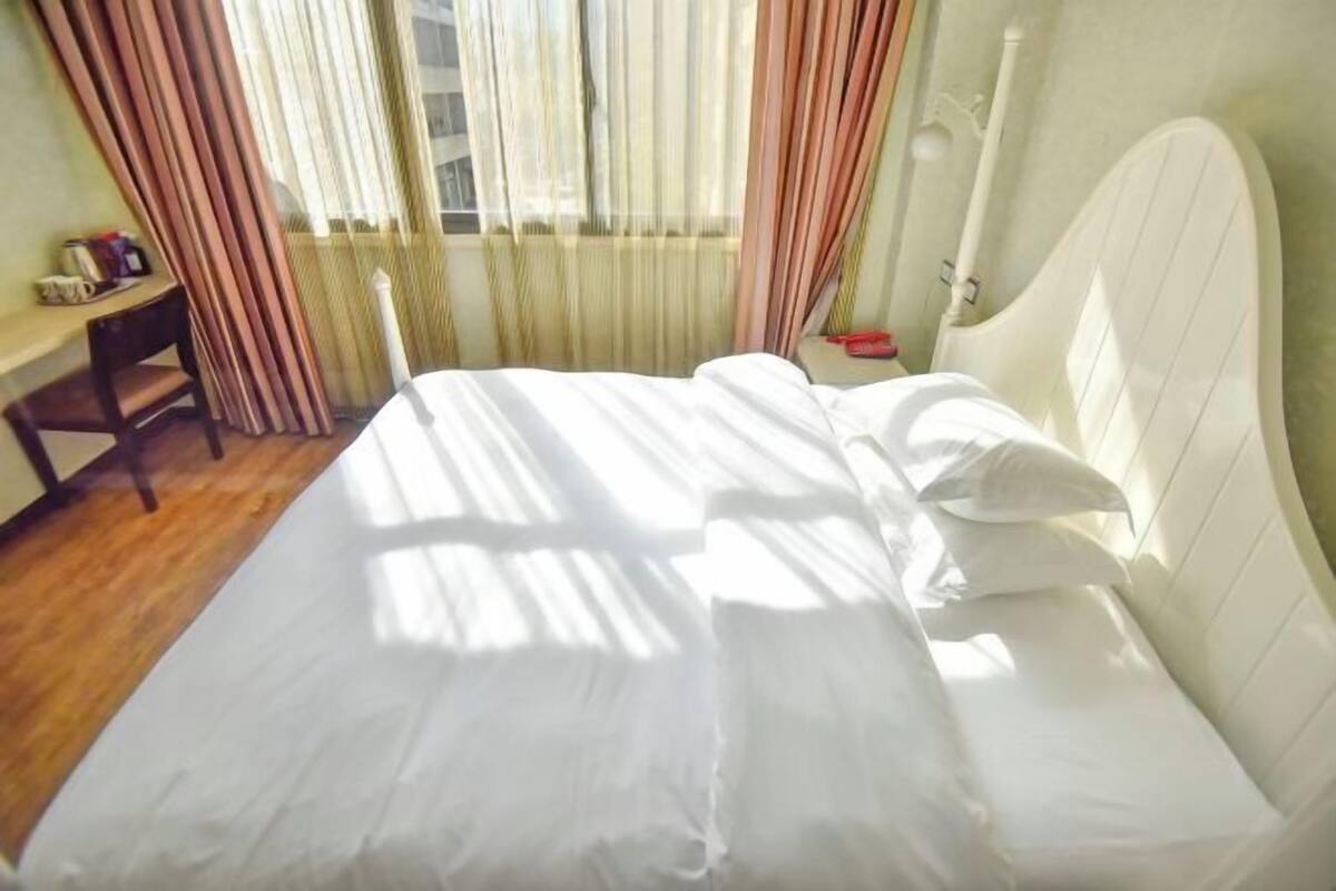 A bed with white linens, a bedside table, a chair, a lamp, and a window with curtains.