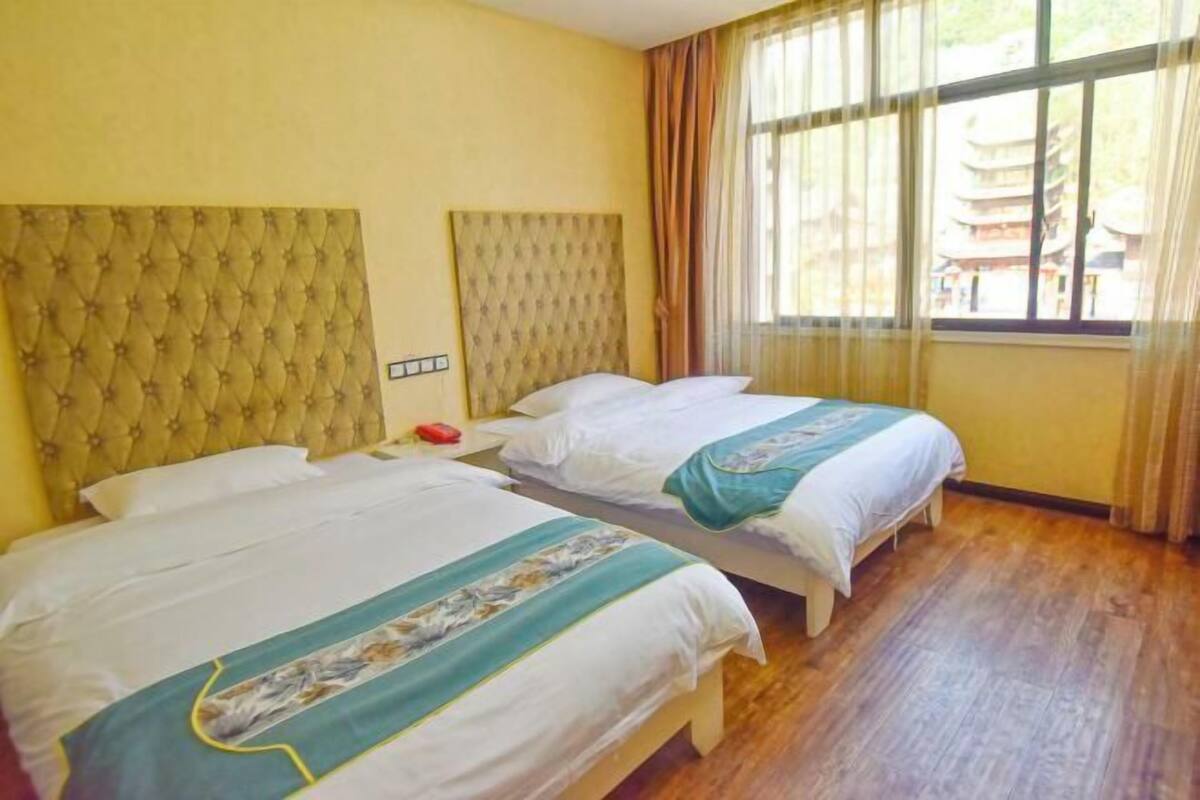 A hotel room with two beds, a wooden floor, and a view of traditional architecture through the window.