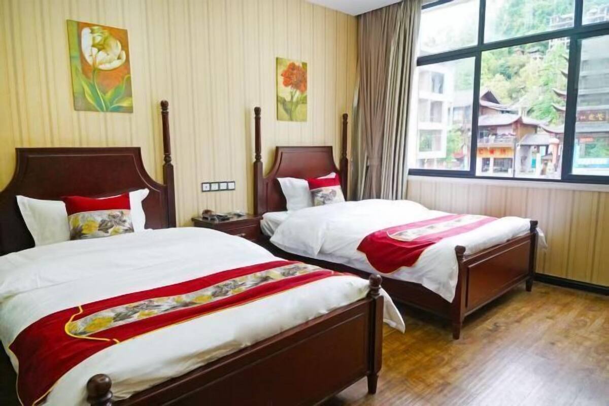 A hotel room with two wooden beds, a large window with a view of traditional buildings, and artwork on the walls.